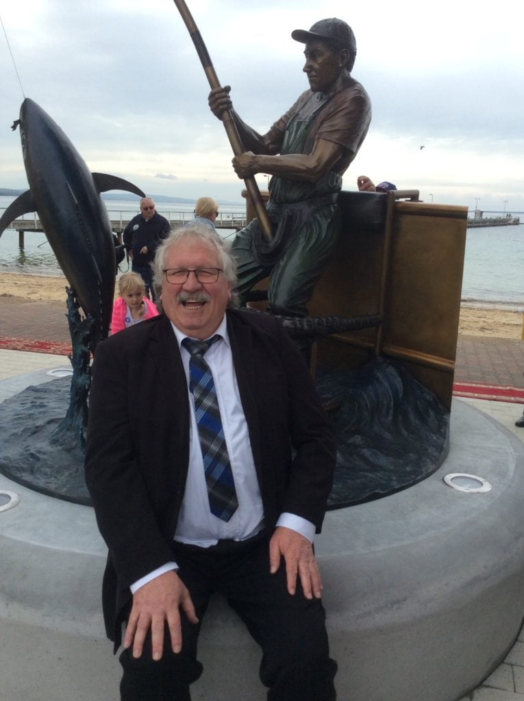 Sculptor Ken Martin sits in front of the Tuna Poler staue he created